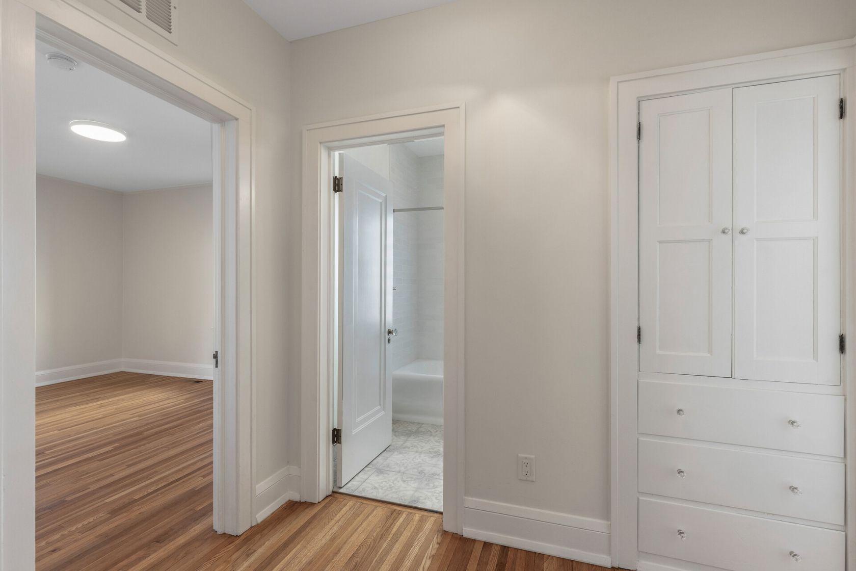 Bedroom hall with restored hardwood, built-in linen, and new bath